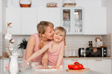 Mom and daughter cook in the kitchen. A young woman cooks with her child in the kitchen at home. Girls in pink clothes cook pizza. Happy and cheerful mom and daughter