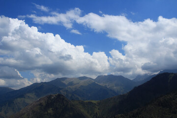 Above mountain ranges and peaks, low dense clouds on the Kok Zhailau plateau, blue sky, summer, sunny