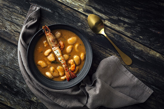 From above of appetizing cream soup with white beans and langoustines served in bowl and placed on wooden tabletop near napkin in kitchen
