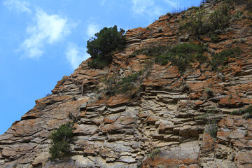 On a large slope of a rocky stepped mountain near the Assy plateau, small bushes grow, cracked stones with red lichen, a sky with clouds, summer, sunny