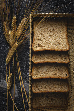 Top view of fresh homemade rye bread near knife in wicker basket and wheat spikes on table