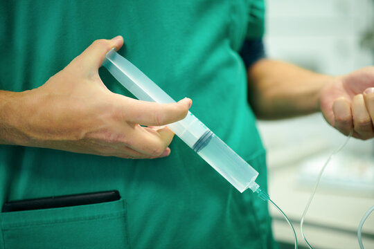 Crop anonymous doctor in medical uniform filling infusion drip with syringe while preparing intravenous procedure in hospital