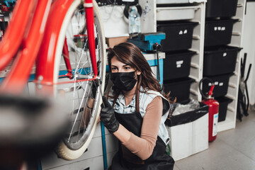 Beautiful young female mechanic with face protective mask repairing bicycles in a workshop..