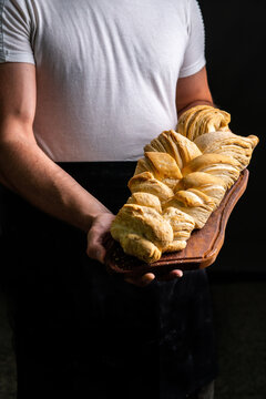 Crop female baker holding wooden board with puff braided bun of bread in dark