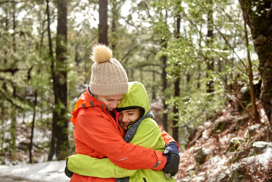 Side view happy smiling siblings in warm clothes embracing each other while spending peaceful winter day in snowy frozen woods