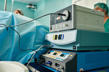 From below of anonymous female doctors standing near coagulator and endoscopic equipment placed near operating table during medical procedure