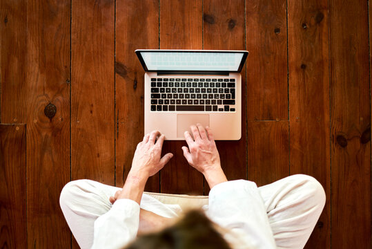 From above cropped unrecognizable concentrated male sitting with crossed legs browsing on netbook in meditation room while practicing yoga