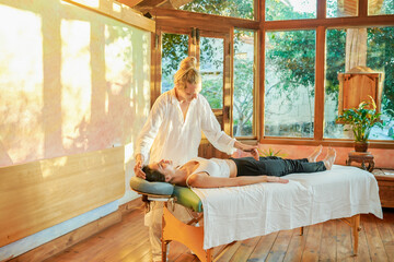 Healer practicing palm healing technique for female client lying on couch during spiritual practice for filling with harmony and energy