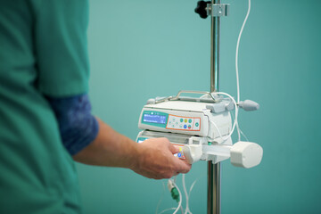 Side view of crop anonymous doctor in medical uniform controlling IV on modern infusion pump in operating room