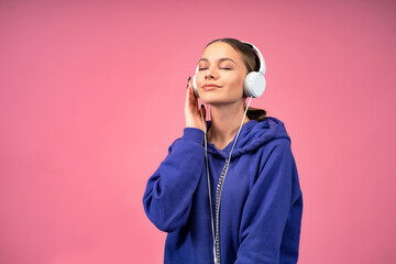 People, music, emotions. A romantic, positive, carefree woman listens to a playlist with headphones to a loud song and has fun. Pensive girl on pink isolated background