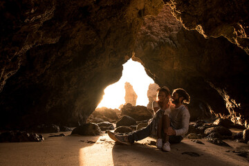 Side view of man and woman smiling at each other while sitting in entrance of cave near sea in Algar seco caves in Algarve, Portugal
