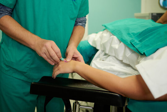 Crop unrecognizable medical assistants inserting intravenous catheter in hand on anonymous patient lying on couch in operating room