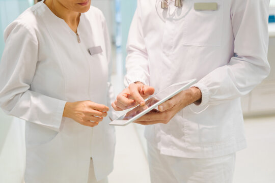 crop anonymous dentists in medical robes examining teeth condition on x ray scan on tablet while working together in modern dental clinic