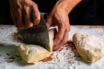 From above of man dividing raw bread dough with scraper on wooden table in baker