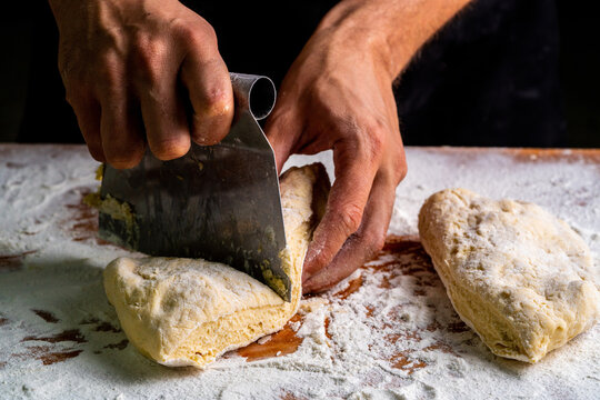 From above of man dividing raw bread dough with scraper on wooden table in baker