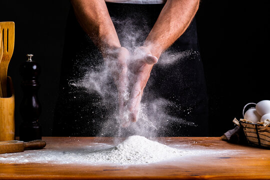 Faceless male baker clapping hands in flour while making bread dough with wheat flour and eggs at table