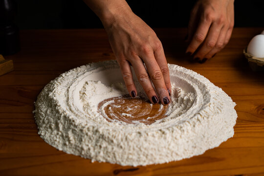 High angle of crop female making hollow in pile of wheat flour on wooden table in bakery