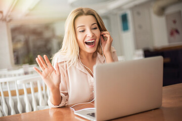 Young woman in cafe sitting having video call waving to camera smiling cheerful