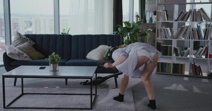Attractive young woman in sexy outfit using vacuumm cleaner equipment tidying her apartment. Sexy housewife. Concept for seduction.