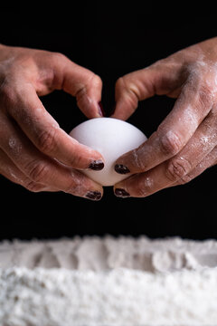 Faceless female baker breaking raw chicken egg into sifted flour pile on table cooking bread