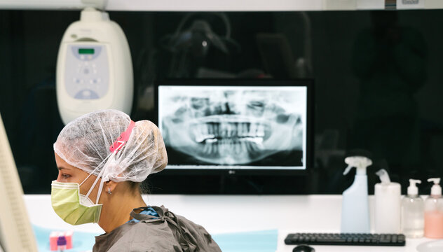 Side view of competent female dentist in medical mask and uniform examining doing X ray of teeth of patient in modern clinic