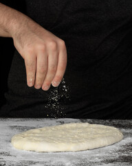 Men's hands or chef sprinkling flour in batter or dough to prepare and bake pizza or bread