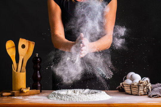 Faceless female baker clapping hands in flour while making bread dough with wheat flour and eggs at table