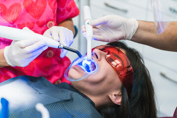 Crop anonymous dentist in gloves using dental ultraviolet curing light tool during procedure with patient in clinic