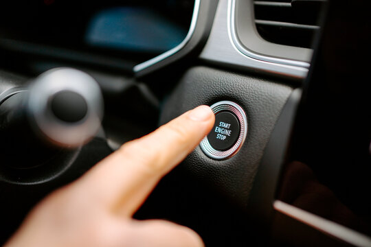 Closeup of crop anonymous male pressing Start Engine Stop button while sitting in modern car before driving