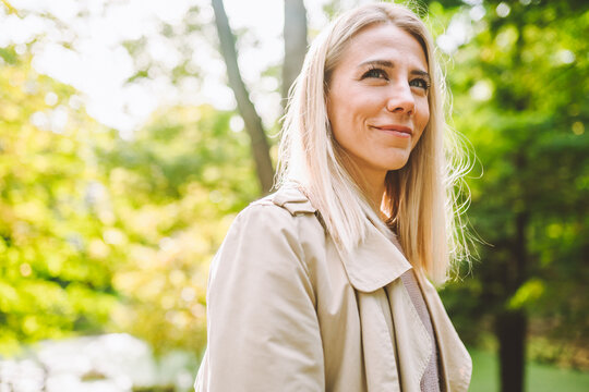 Caucasian blonde woman smiling happily on sunny summer or spring day outside walking in park.