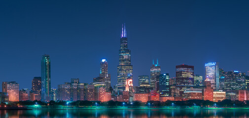 Night cityscape of Chicago with contemporary buildings and towers illuminated by colorful lights reflecting in calm lake water