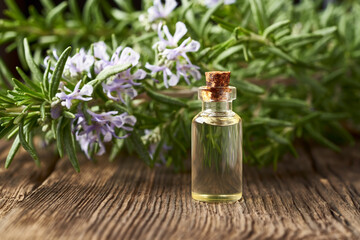 A bottle of essential oil with fresh blooming rosemary twigs