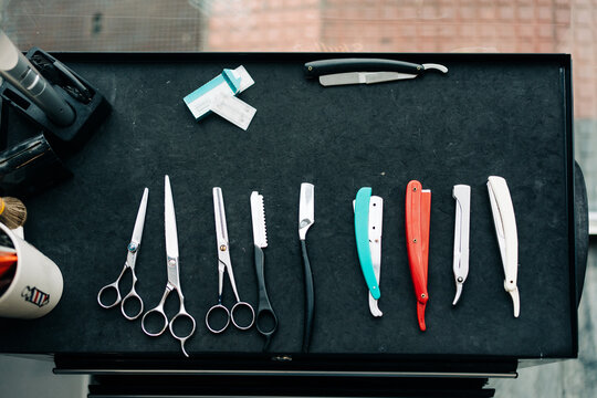 Top view of assorted scissors near straight razors with sharp metal blades on table in hairdressing salon