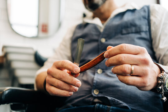 Crop unrecognizable male stylist holding straight razor with sharp blade in beauty salon in daytime