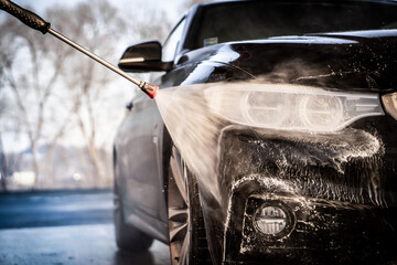 A man washes his luxury black sports car in a manual car wash.