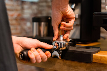Crop unrecognizable barista pressing coffee in portafilter with tamper while preparing beverage in cafe