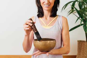 Crop smiling female playing on Tibetan singing bowl while for relax and meditation in studio