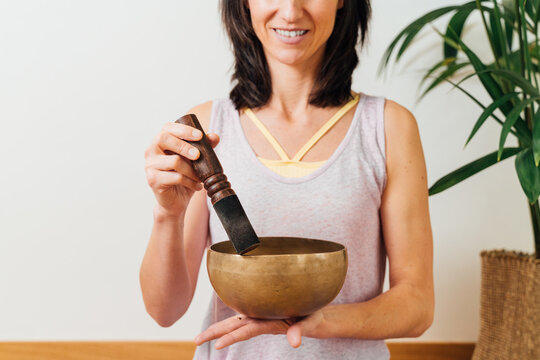 Crop smiling female playing on Tibetan singing bowl while for relax and meditation in studio