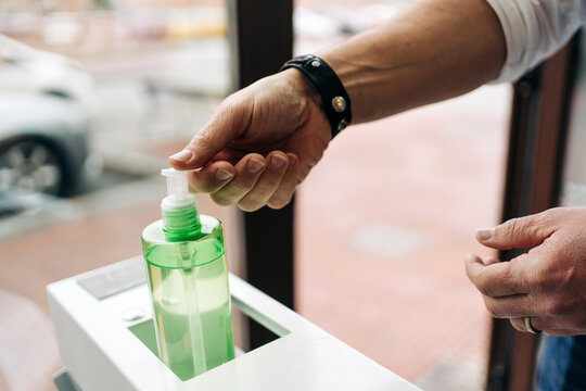 Crop anonymous male barber in wristwatch applying antibacterial gel on hands at work in beauty salon