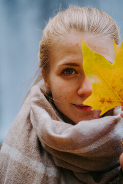 Content female in warm scarf covering eye with yellow maple leaf and looking at camera