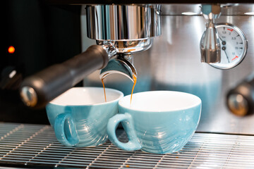 Professional coffee machine pouring coffee into small ceramic cups in coffeehouse with contemporary equipment