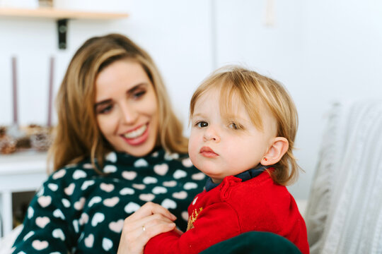 Cute little child sitting on sofa with smiling mother at home and looking at camera