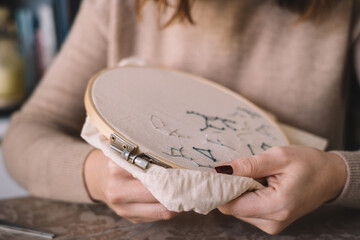 Side view of crop female with hoop and threads embroidering star constellations while sitting at table in light workshop