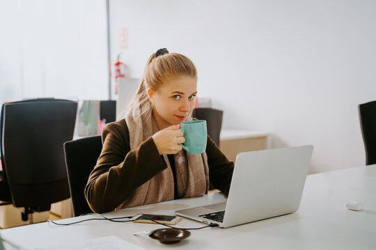 Blonde business woman working in front of computer in an office with a cup of coffee