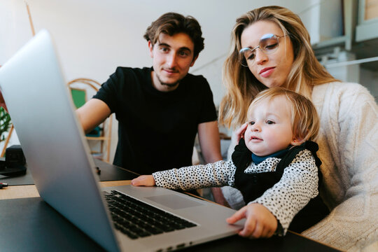 Young couple and toddler sitting at table and watching movie together while spending weekend at home
