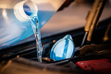 Pouring blue antifreeze liquid for washing car screen.