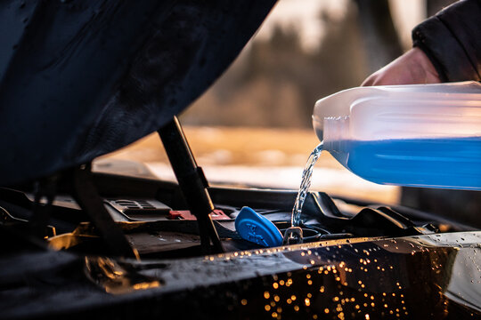Pouring blue antifreeze liquid for washing car screen.