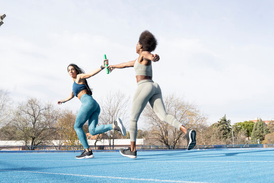 Fit multiracial female athletes passing baton while running along track at stadium during relay race