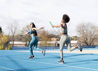 Fit multiracial female athletes passing baton while running along track at stadium during relay race