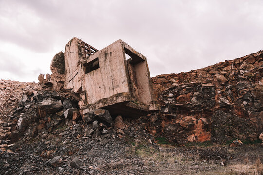 Piece of destroyed cement building on open pit with rough stones under cloudy sky in daylight